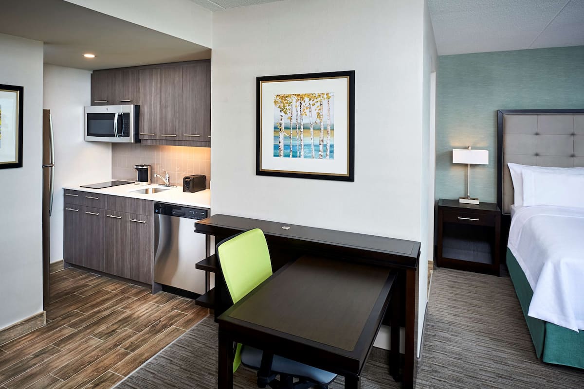 Ein gemütliches Hotelzimmer mit Küchenzeile, Essbereich, Bett und einem gerahmten Kunstwerk an der Wand.