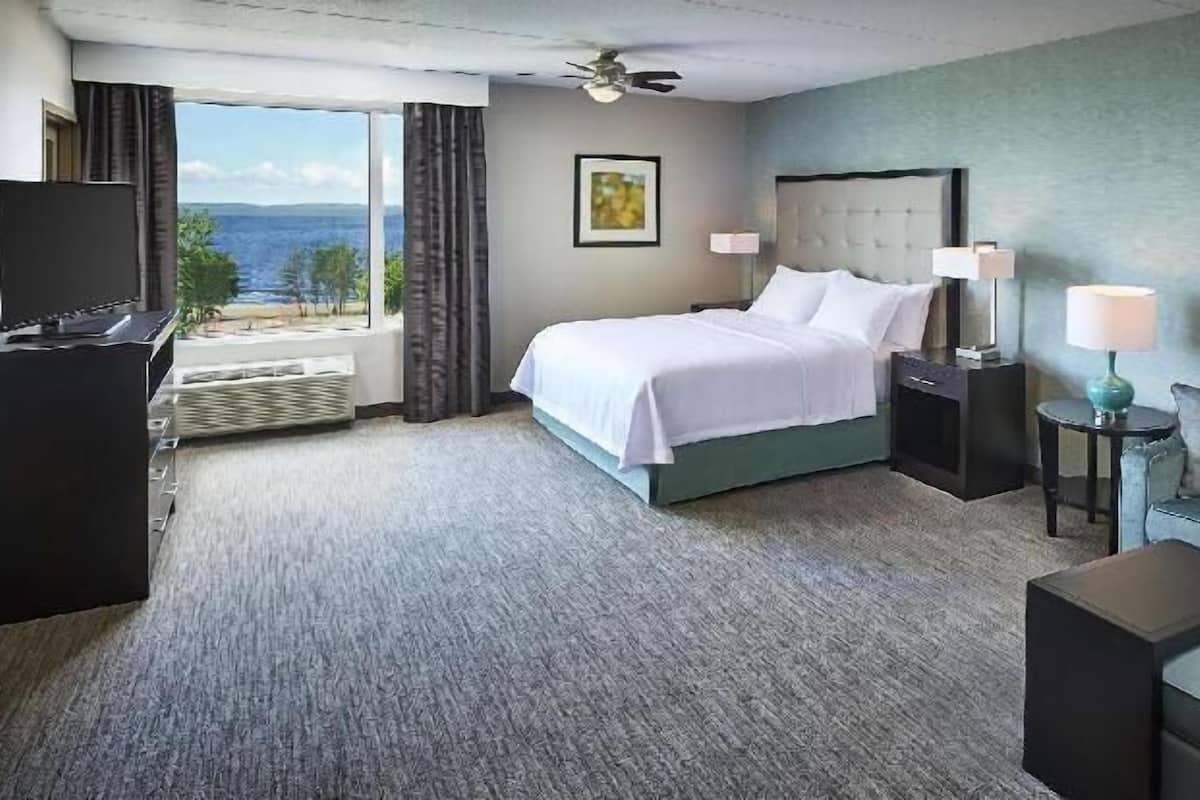 Ein Hotelzimmer mit Bett, Fernseher, Sofa, Couchtisch, Schreibtisch und Blick ins Freie.
