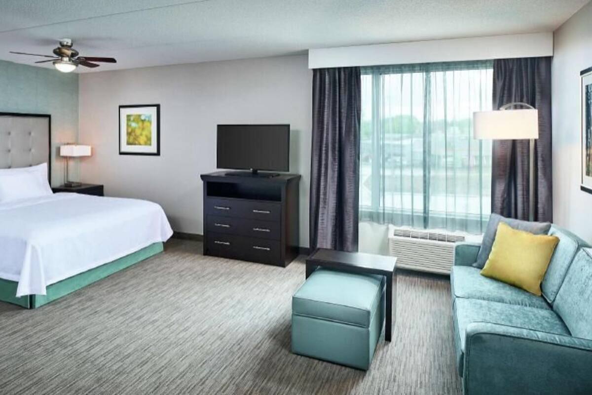 Ein Hotelzimmer mit Bett, Fernseher, Sofa, Schreibtisch und einem Fenster mit Vorhängen.