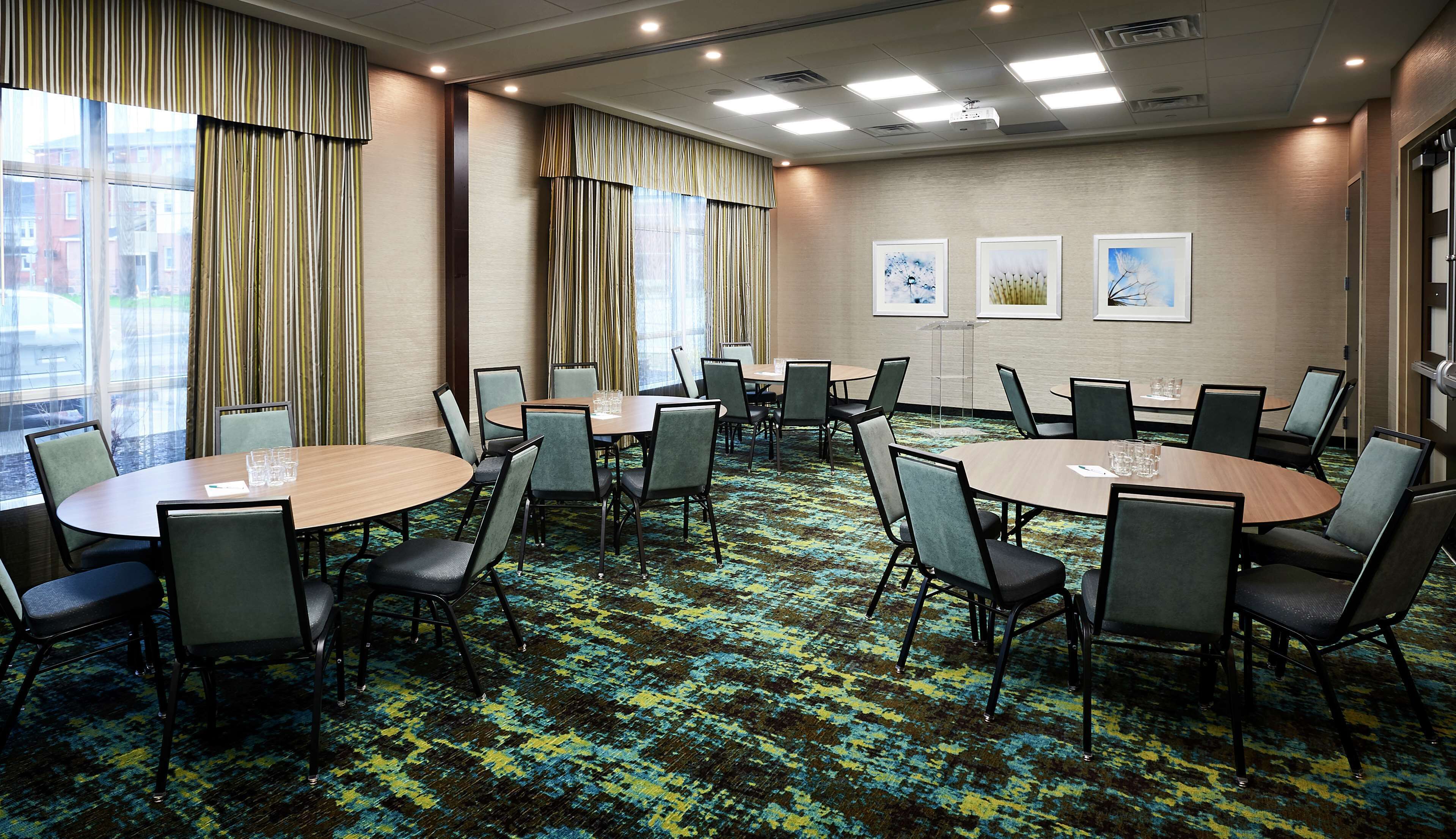 A conference room with round tables and chairs, large windows with curtains, and artwork on the walls.