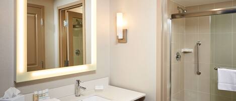 A modern bathroom with a large mirror, a sink with toiletries, a towel rack, and a glass-enclosed shower.