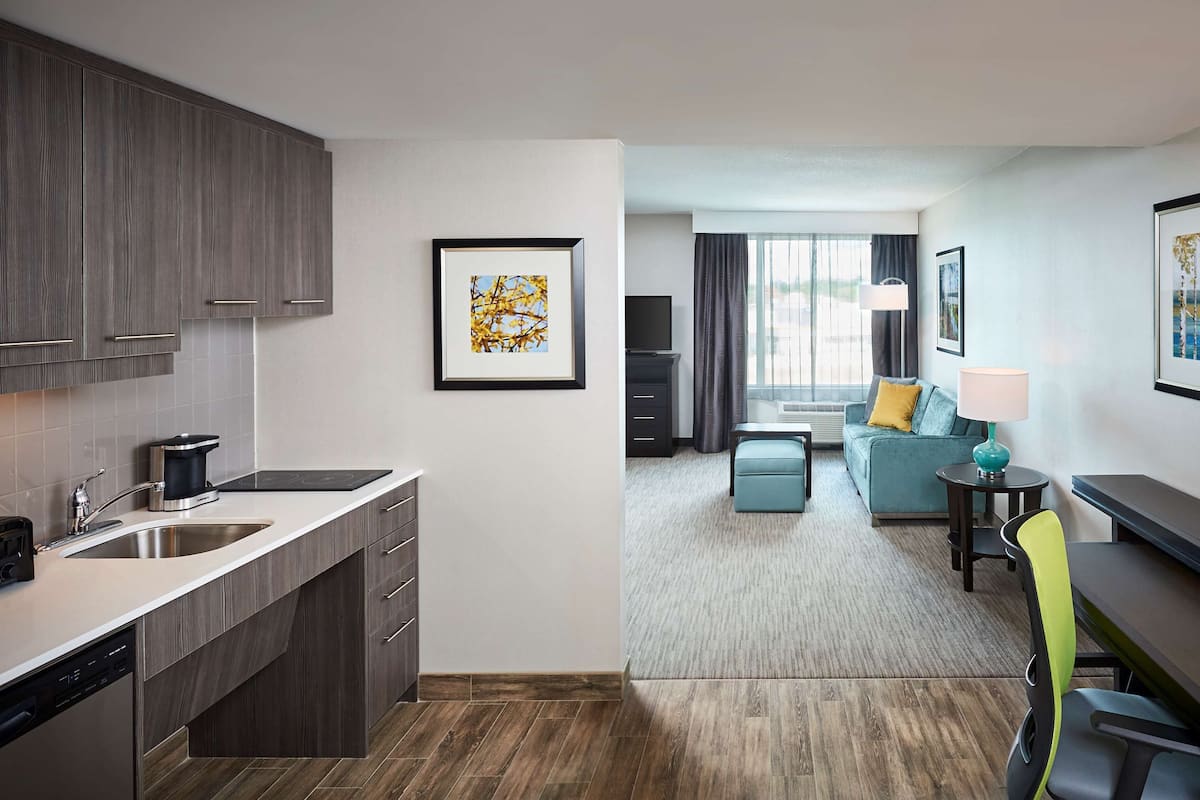 Ein modernes Hotelzimmer mit einer Küchenzeile, einer Wohnbereits mit Sofa und Fernseher sowie einem Essbereich mit Tisch und Stühlen.