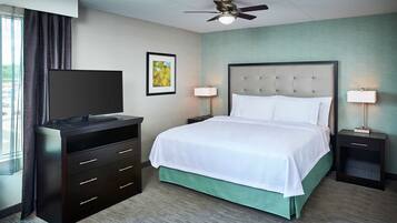 Una habitación de hotel con una cama, un televisor en una cómoda, dos mesitas de noche con lámparas, un ventilador de techo y una ventana con cortinas.