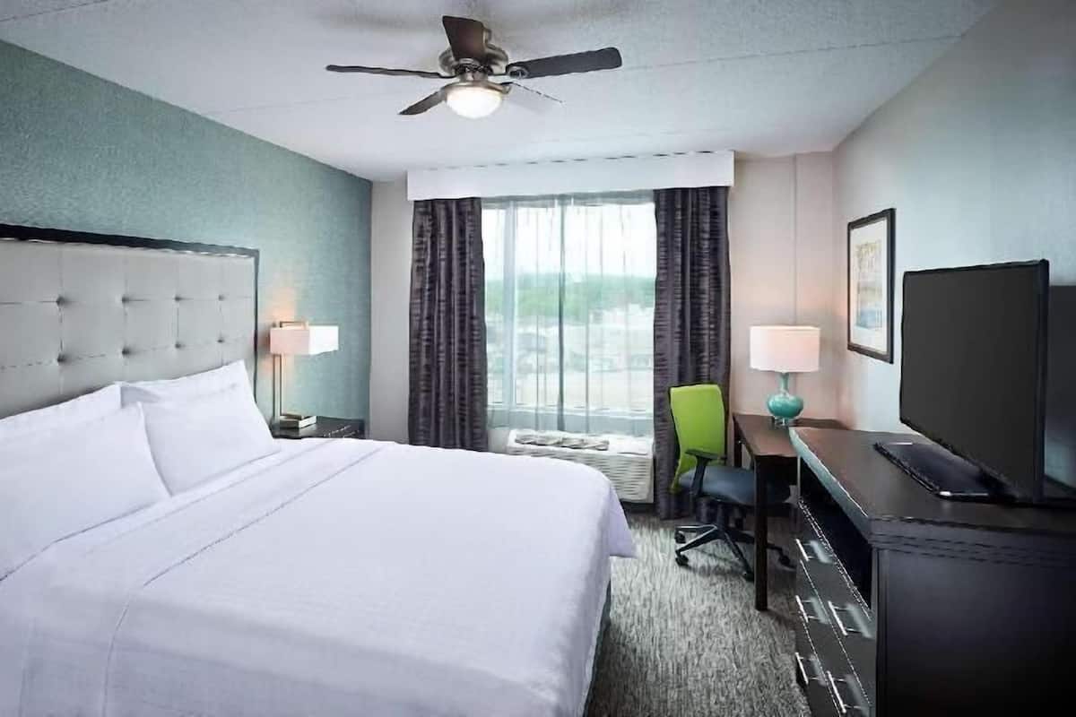 Ein Hotelzimmer mit einem großen Bett, einem Schreibtisch mit Stuhl, einem Deckenventilator und einem Fenster mit Vorhängen.