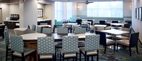 Een restaurant in een hotel met meerdere tafels en stoelen, plafondventilatoren en kroonluchters.