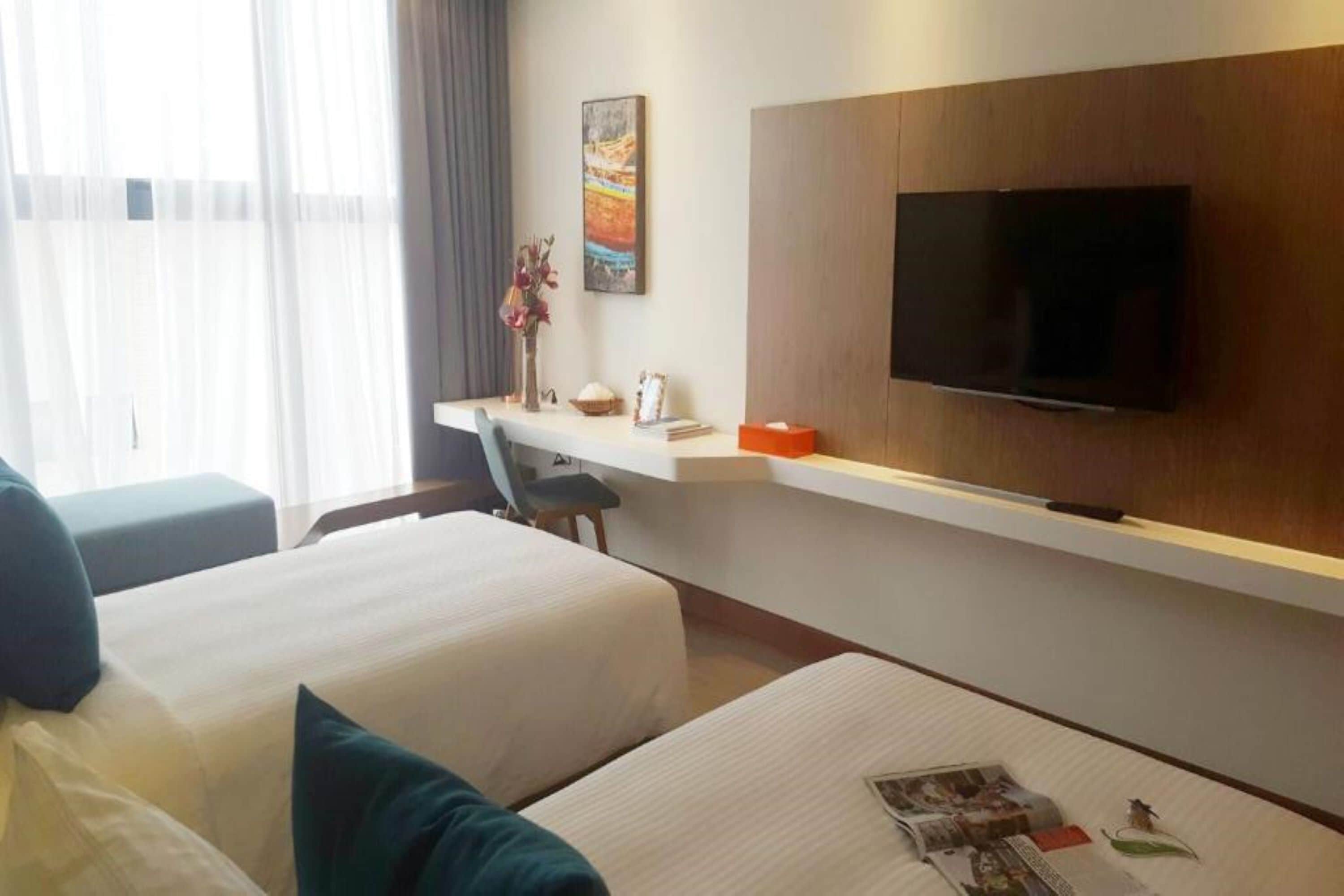 A hotel room with two beds, a desk, a flat-screen TV, and a painting on the wall.