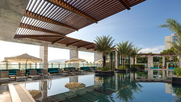 A rooftop infinity pool with lounge chairs and umbrellas, surrounded by palm trees and modern architecture. - Citadines Bayfront Nha Trang (Nha Trang)