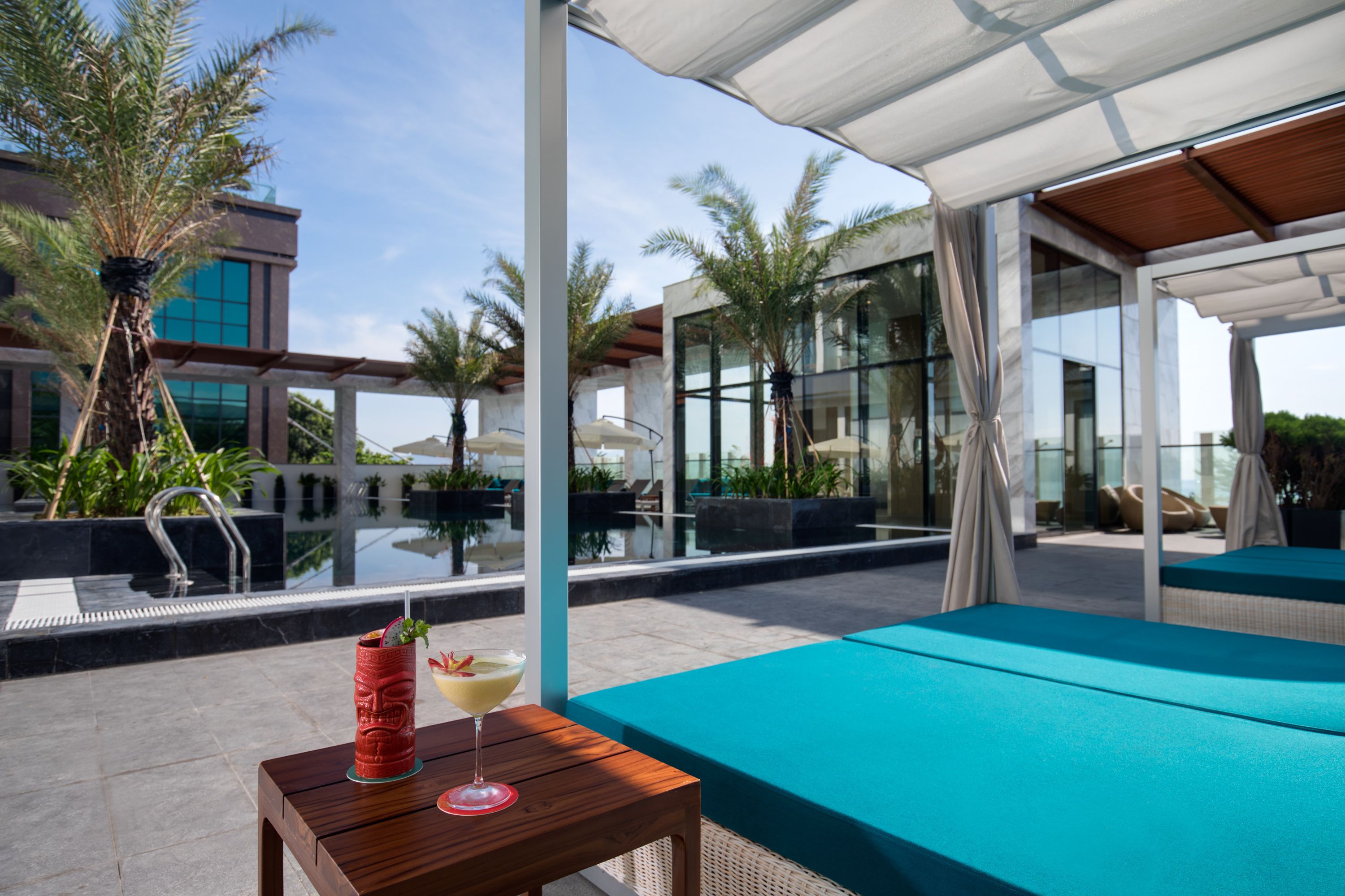 A modern outdoor pool area with a wooden table, a lounge chair, and a glass balustrade.