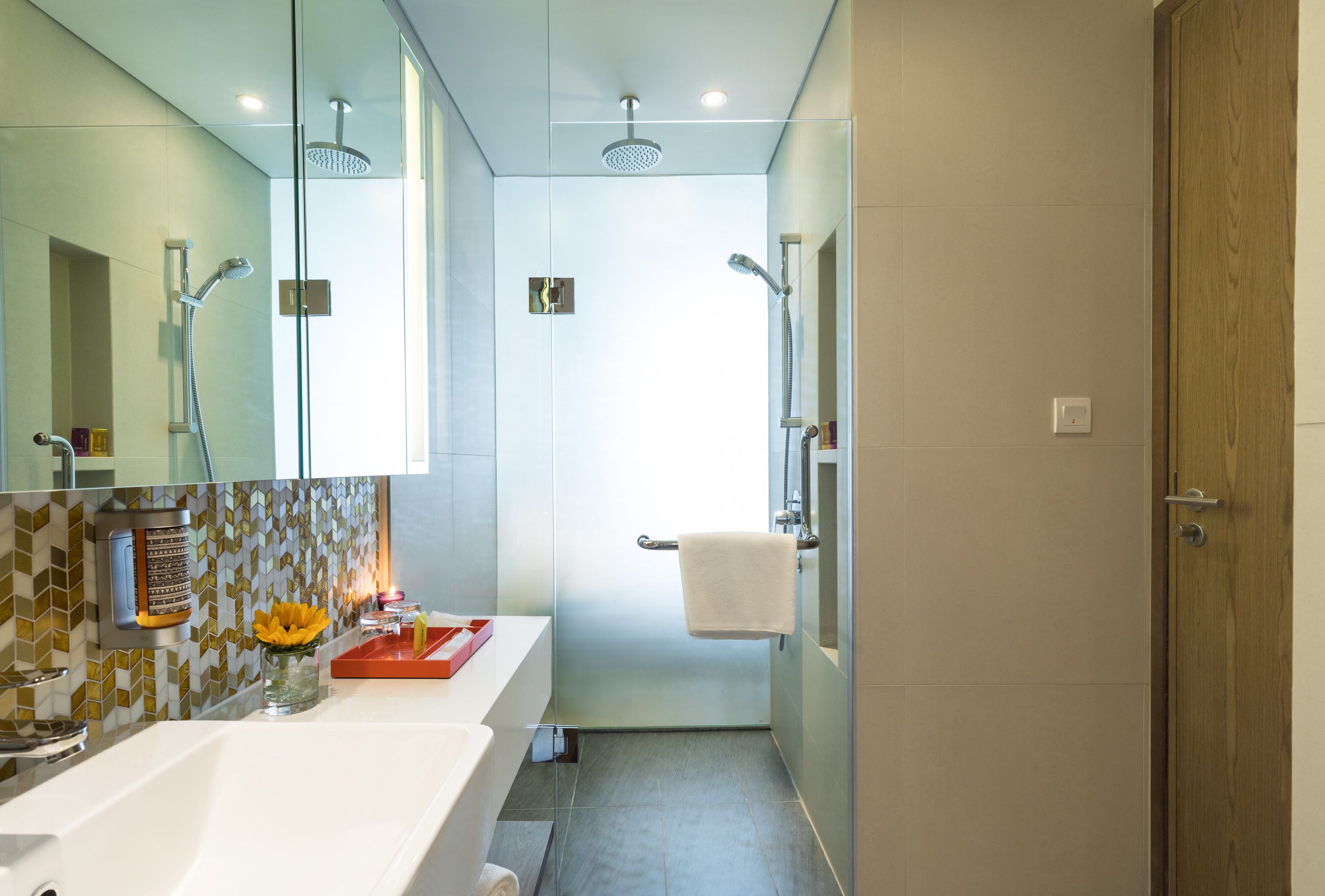 A modern bathroom with a glass shower enclosure, a white sink with a decorative tile backsplash, and a wooden door.