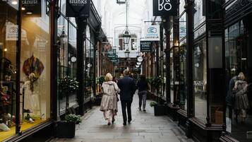 Uma rua estreita só para pedestres, com lojas e cafés, pessoas caminhando e sentadas ao ar livre.