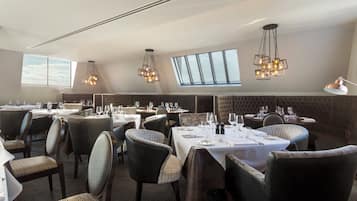Un restaurante con varias mesas, sillas y un techo alto con lámparas colgantes.