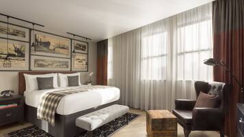 A modern hotel room with a large bed, a sitting area with a chair, a desk, and a box of K-C brand baking powder.