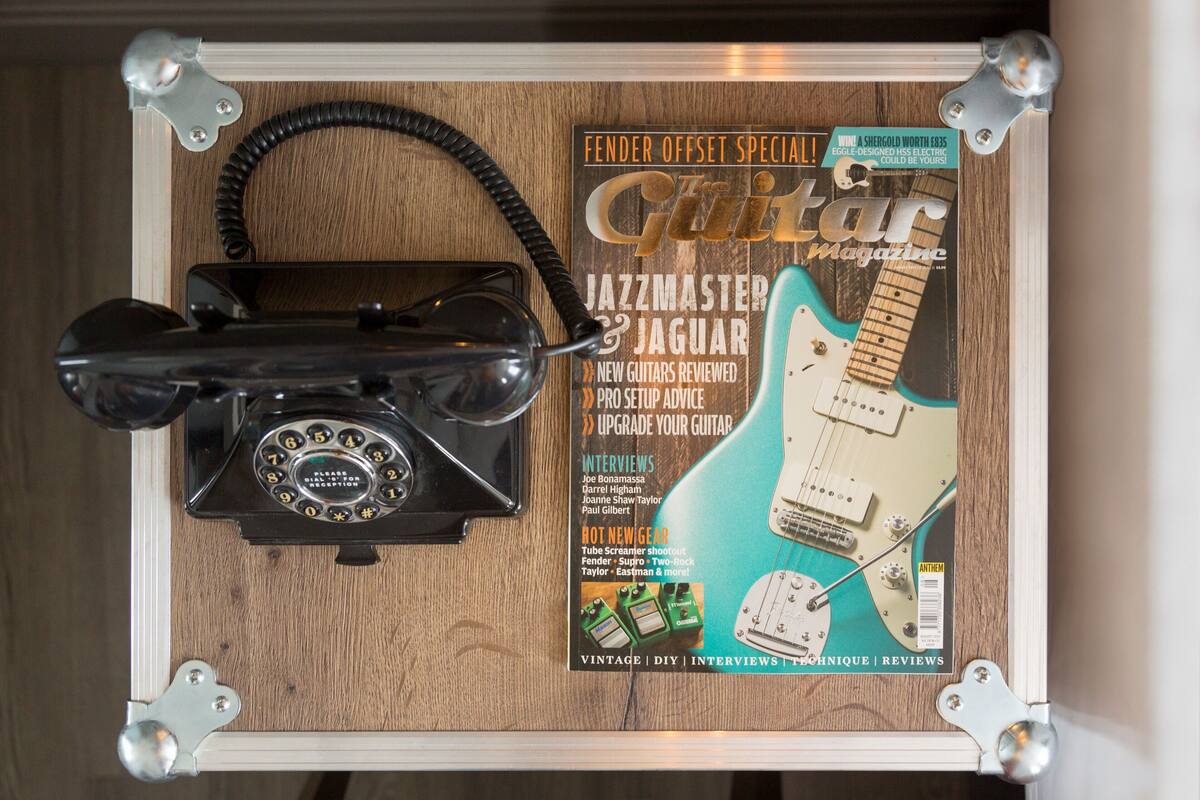 A vintage telephone, a guitar magazine, and a guitar on a wooden surface.