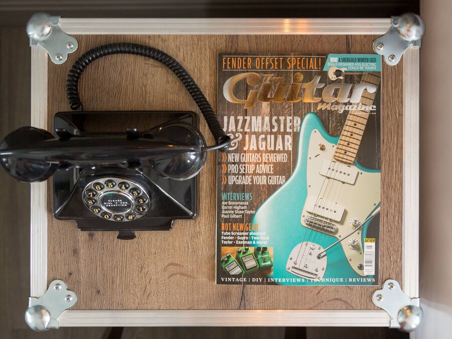 A vintage telephone, a guitar magazine, and a guitar on a wooden surface.