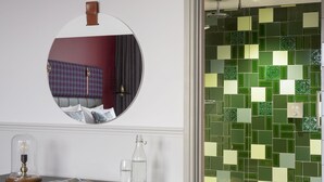 A bathroom with a mirror, a table with a lamp, a bottle, and a glass of water. - Hotel Indigo Cardiff by IHG (Cardiff)