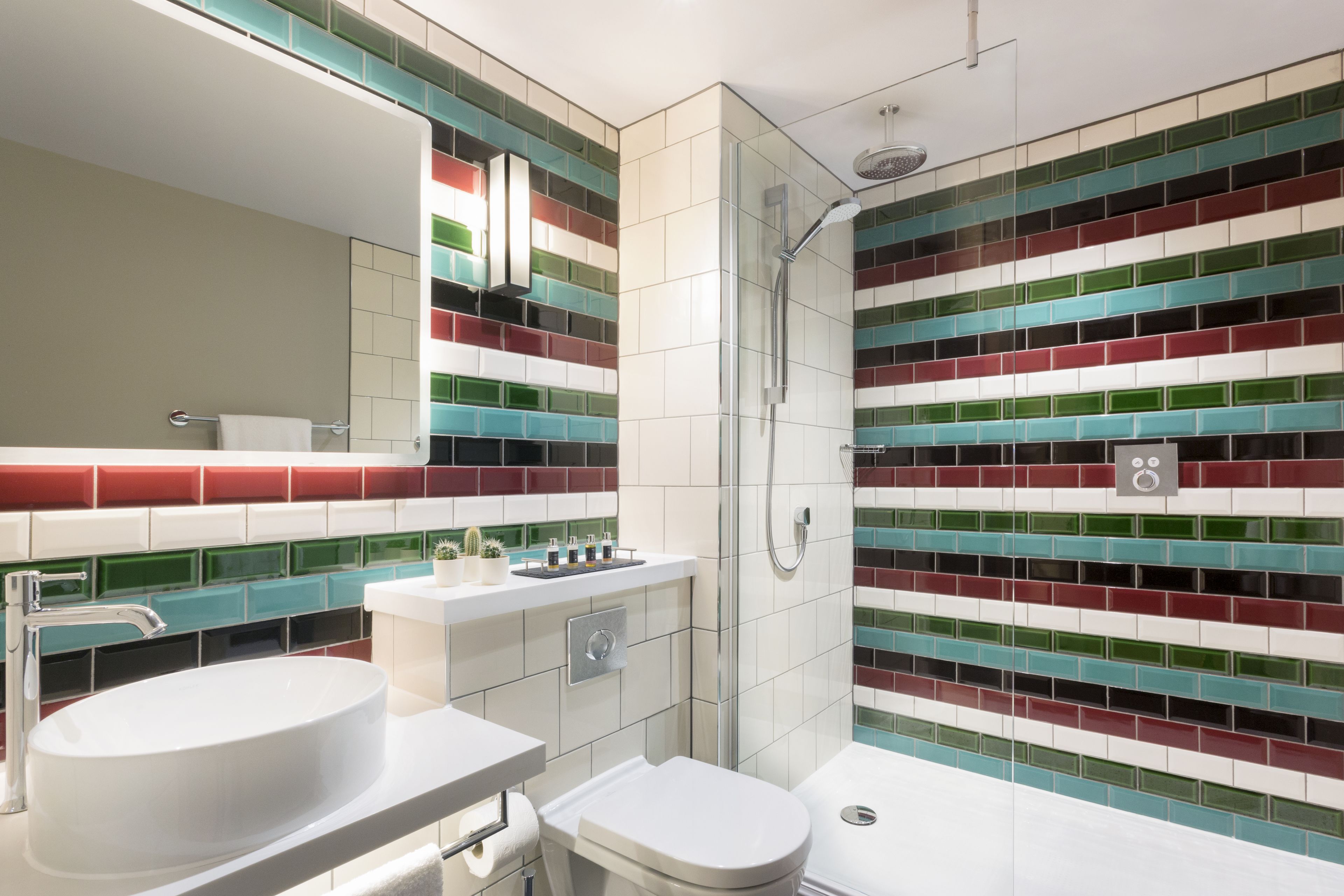 A modern bathroom with a white sink, toilet, and shower. The walls are tiled with multicolored tiles.