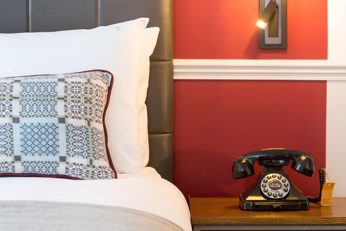 A neatly made bed with patterned pillows, a red wall, a vintage telephone, and a pendant light.