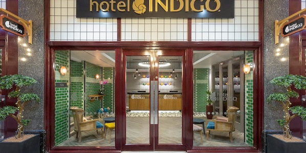 The entrance of Hotel Indigo with a check-in counter, seating area, and potted plants.