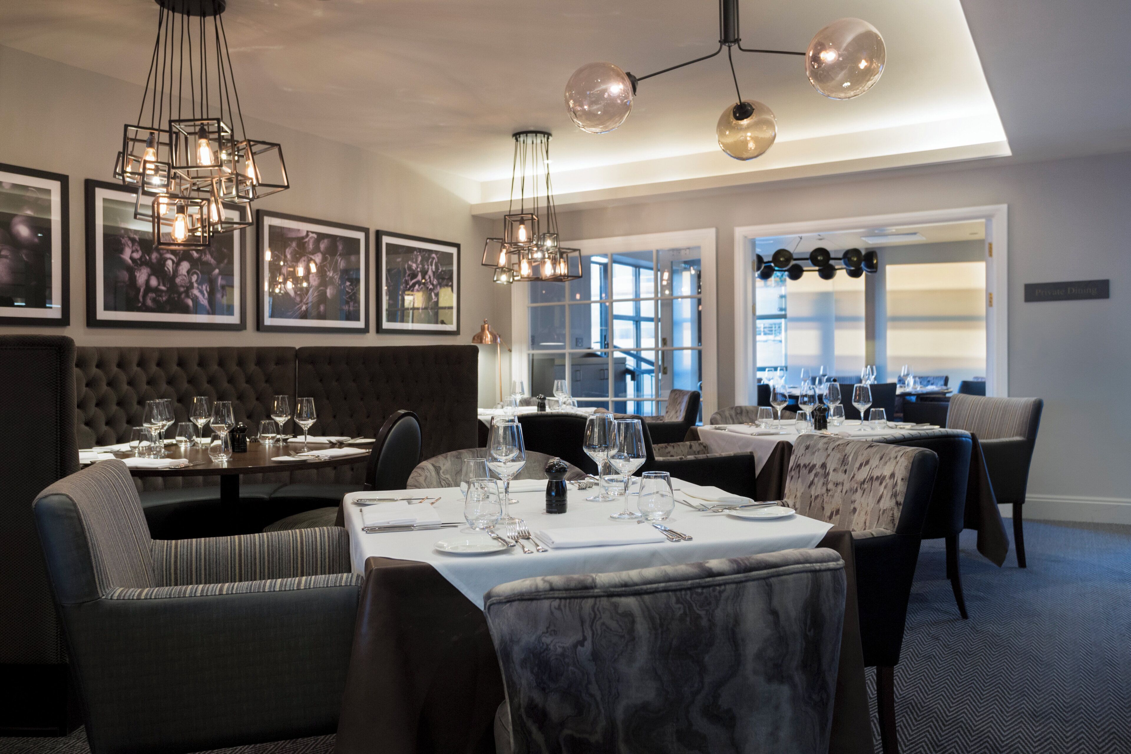 A restaurant interior with multiple dining tables, chairs, and hanging pendant lights.