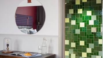 Ein Zimmer mit einem runden Spiegel, einem Tisch mit einer Lampe, einer Flasche und einem Glas Wasser.