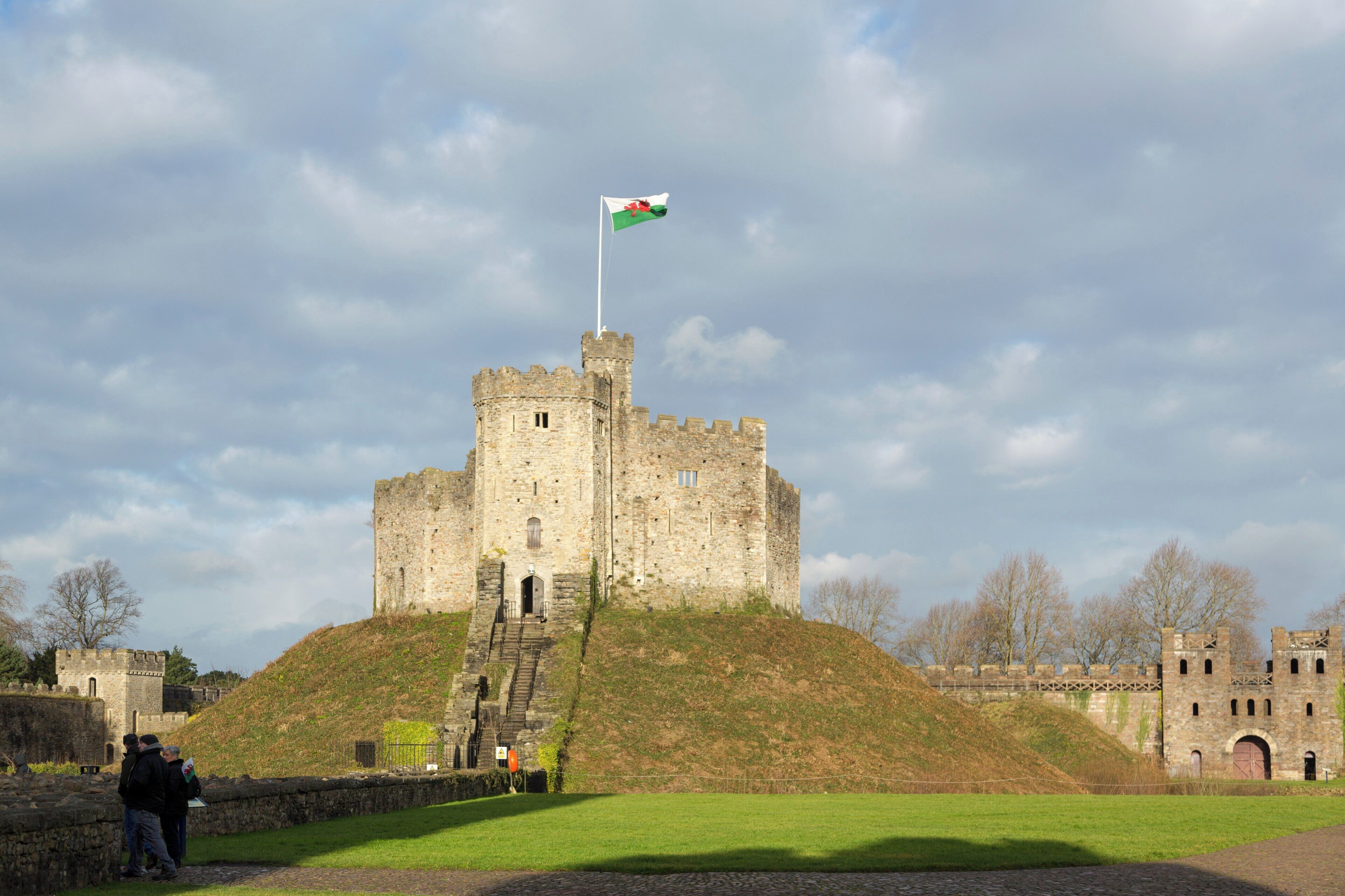 A historic castle with a flagpole, a grassy hill, and a clear sky.