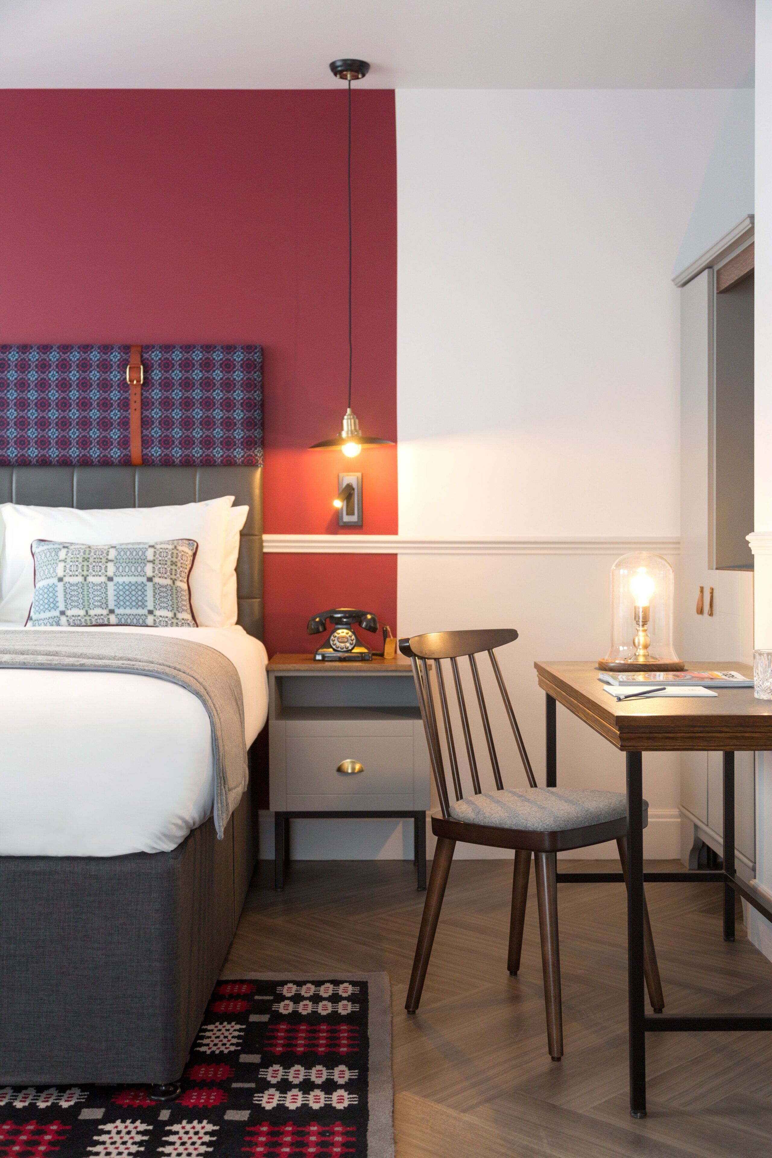 A modern bedroom with a bed, bedside table, chair, and a desk with a lamp.