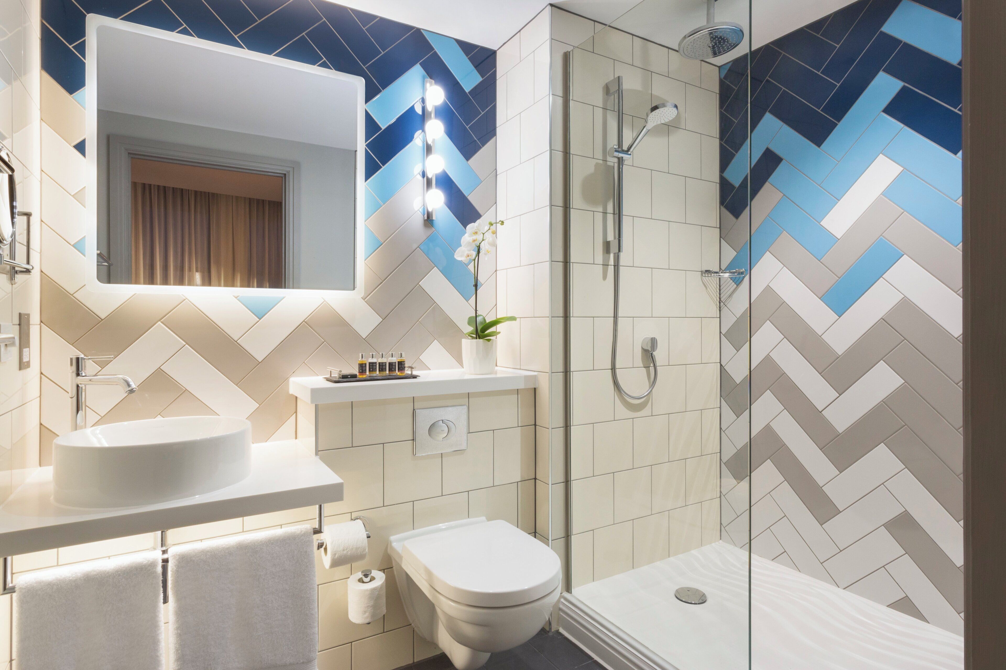 A modern bathroom with a large mirror, a sink, a toilet, and a shower.