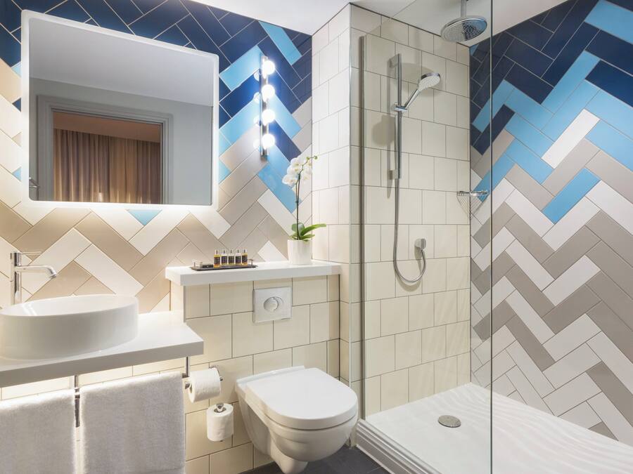 Un baño moderno con un espejo grande, un lavabo, un inodoro y una ducha.