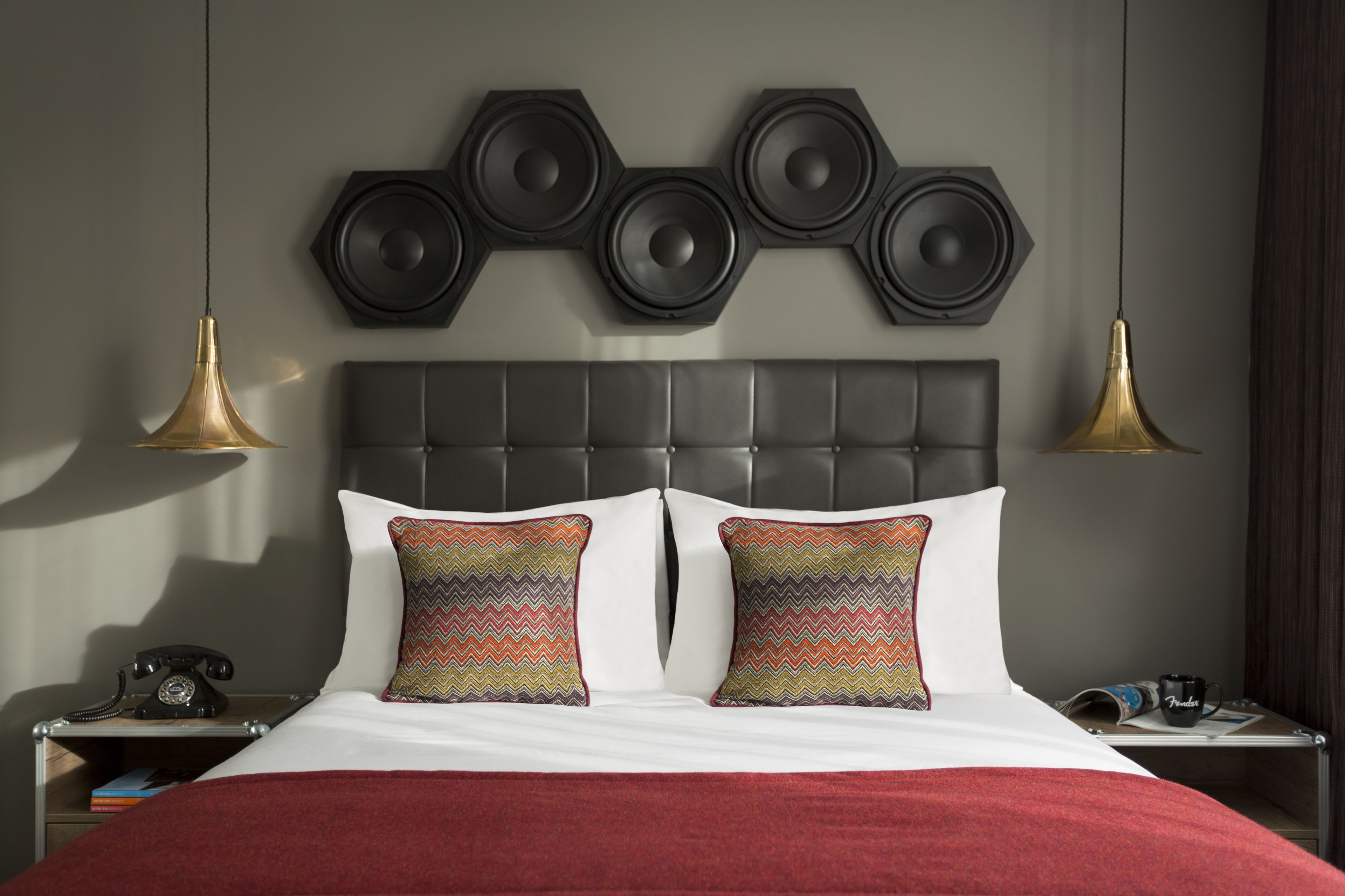 Ein modernes Hotelzimmer mit einem großen Bett, einem Kopfteil mit sechseckigen Lautsprechern und zwei Nachttischlampen.