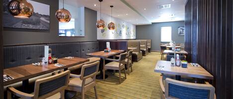 A restaurant with booths and tables, hanging pendant lights, and a striped carpet.