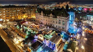 Un edificio histórico con varios niveles y un patio central, rodeado de calles cubiertas de nieve e iluminado con luces festivas.