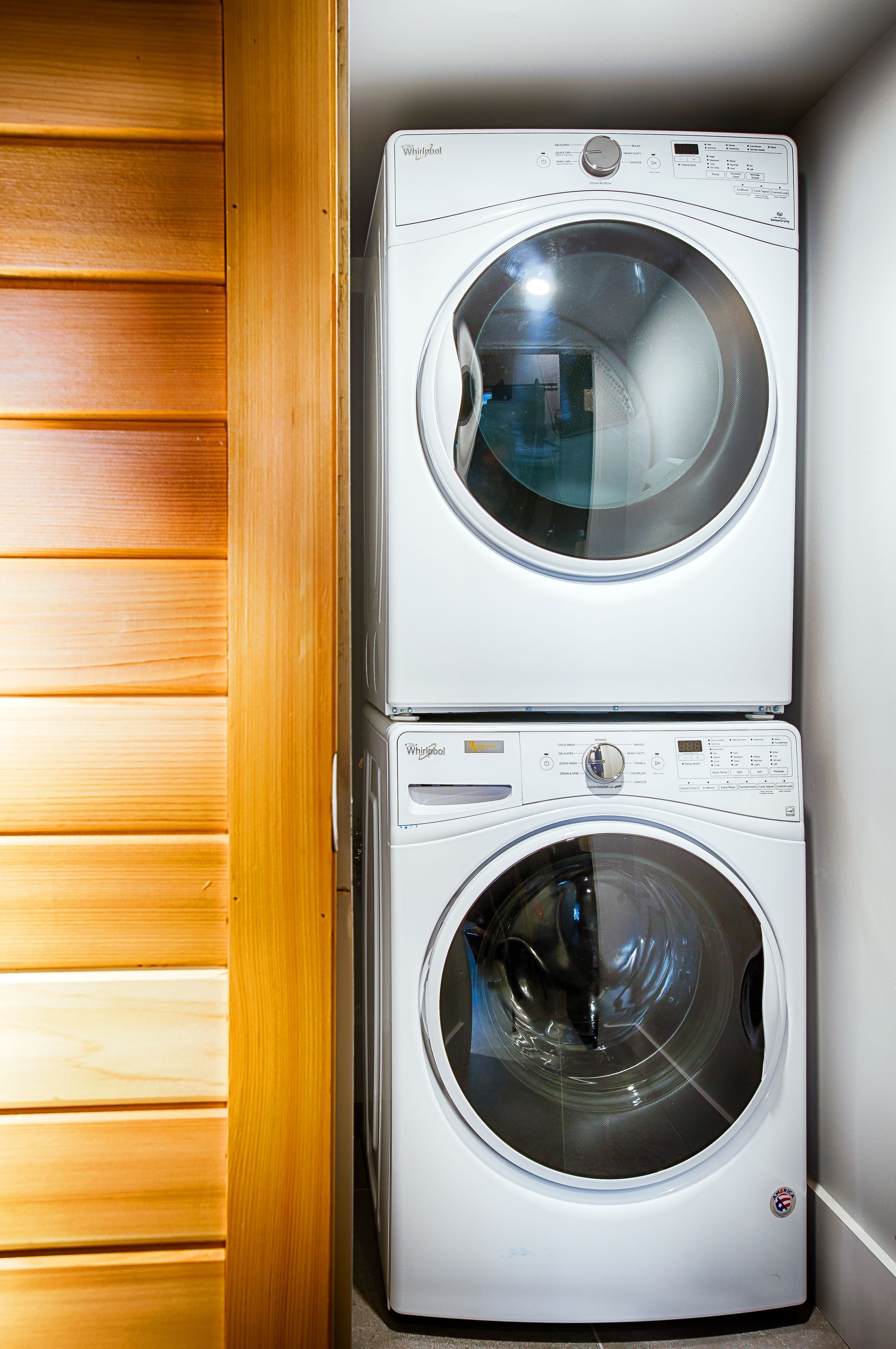 A stacked washer and dryer unit in a laundry room with wooden paneling on one side.