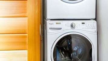 A stacked washer and dryer unit in a laundry room with wooden paneling on one side.