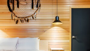 Un dormitorio con cama, cabecera de madera, atrapasueños, lámpara colgante y una puerta.