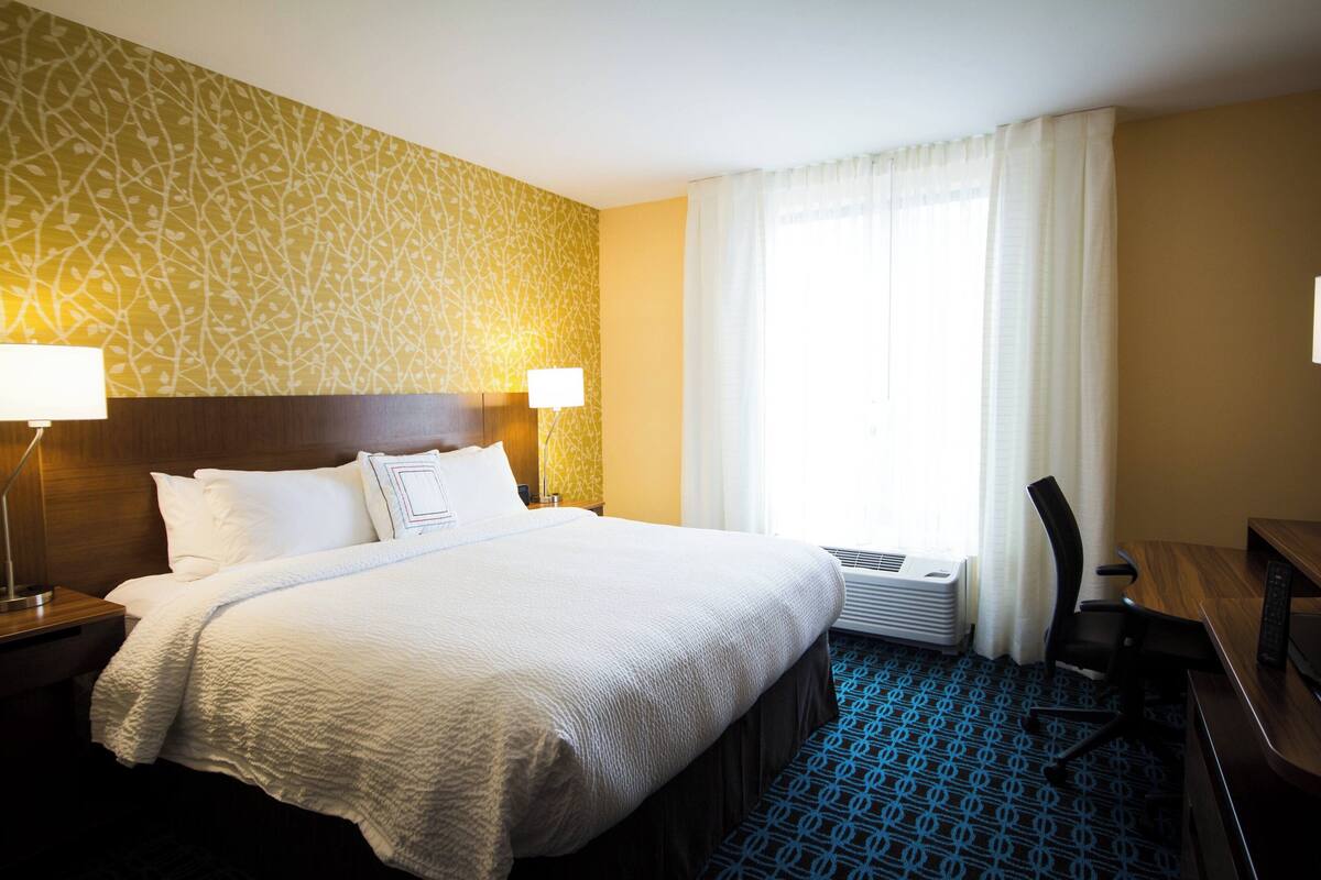 A hotel room with a large bed, two bedside lamps, a desk, and a chair.