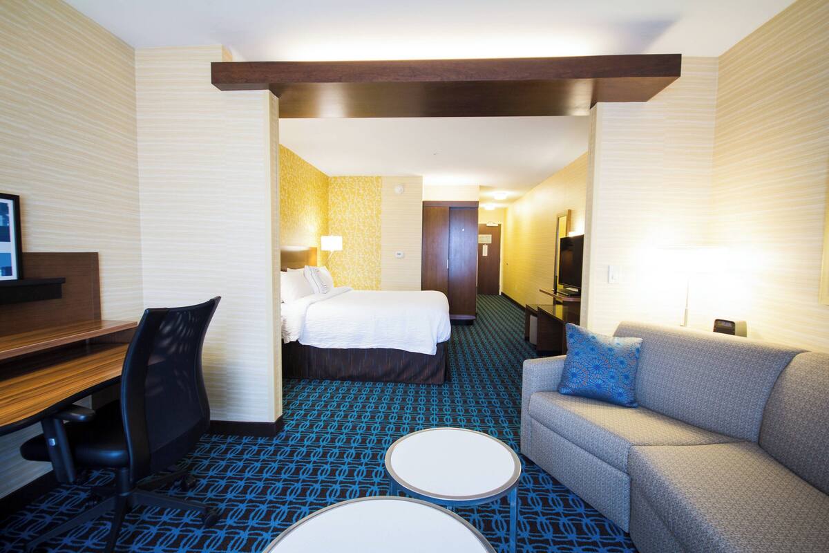 A hotel room with a bed, a desk, a chair, a sofa, and two small tables.