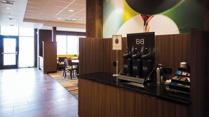 A reception area with a wooden counter, a coffee machine, and a wall with a colorful abstract design. - Fairfield Inn and Suites Denver Northeast Brighton (Brighton)