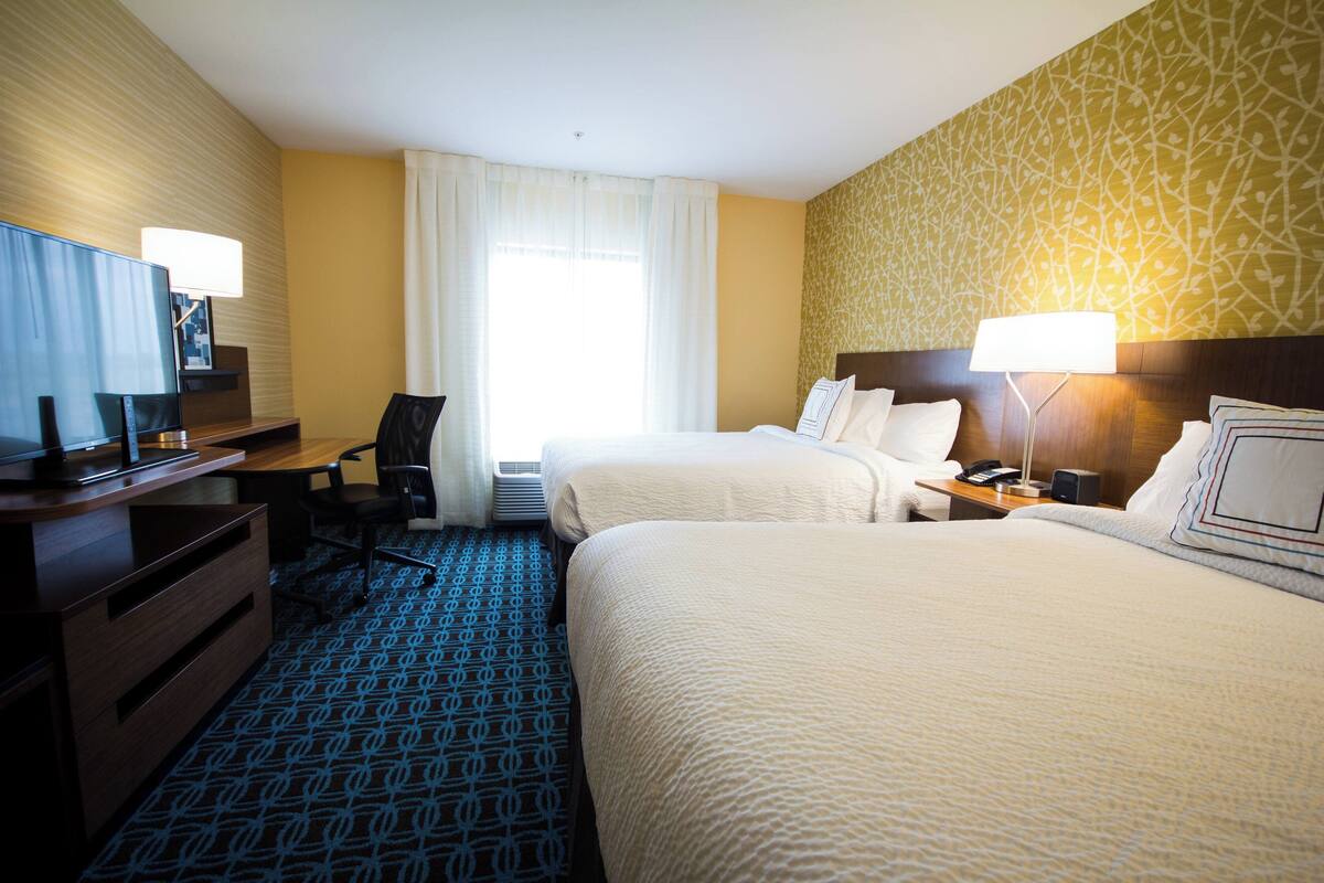 A hotel room with two beds, a desk with a computer, a chair, and a television.