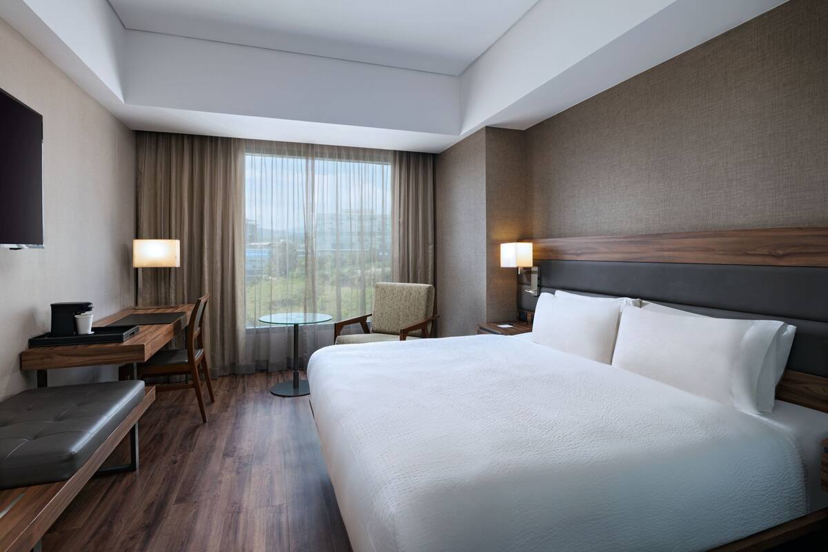 A hotel room with a large bed, a desk, a chair, a small table, and a TV.