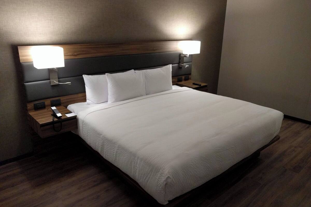 Un lit bien fait, avec du linge de lit blanc, deux tables de chevet avec des lampes et une tête de lit en bois.