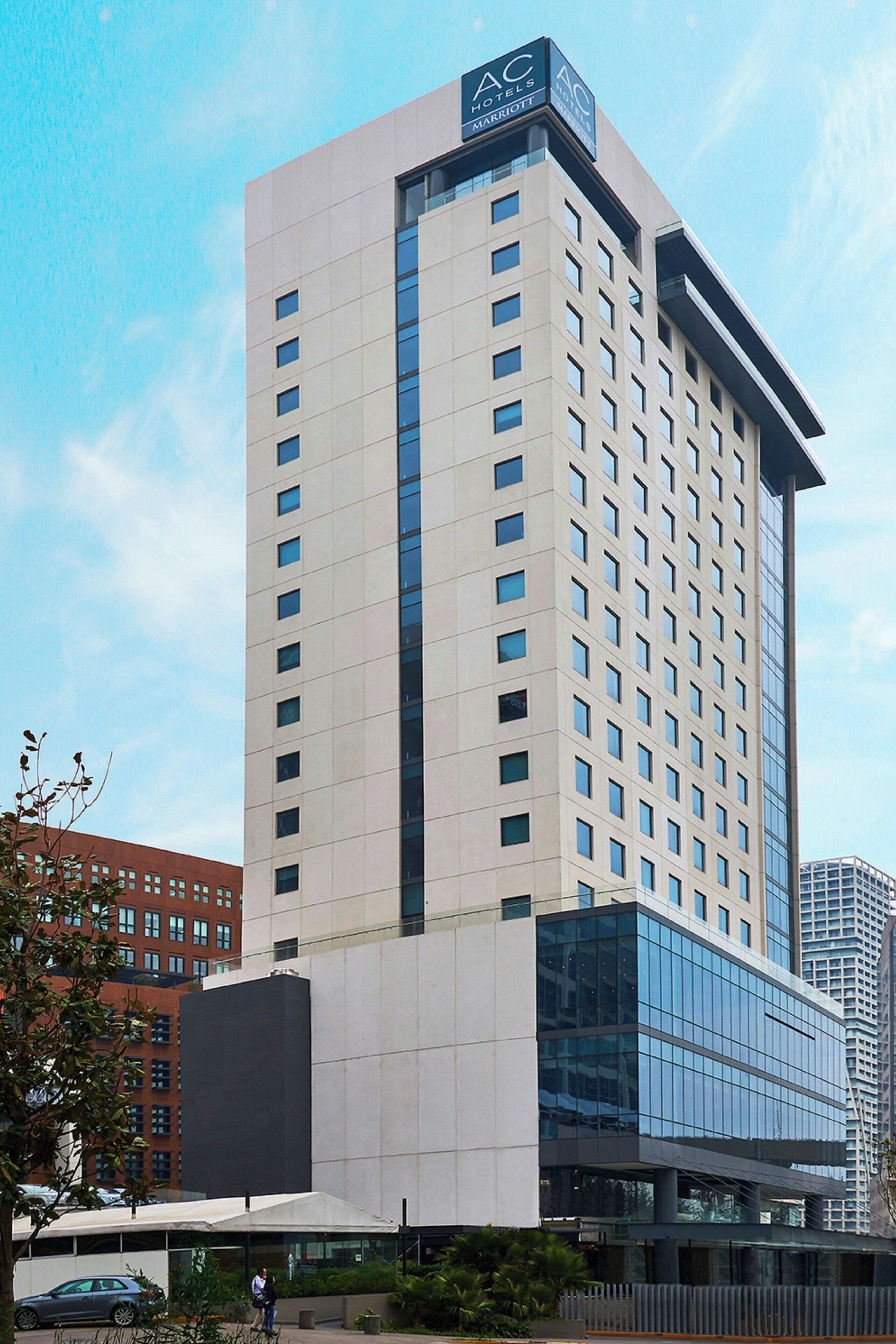 Um edifício de hotel alto com design moderno, exibindo um logotipo AC bem visível no topo.