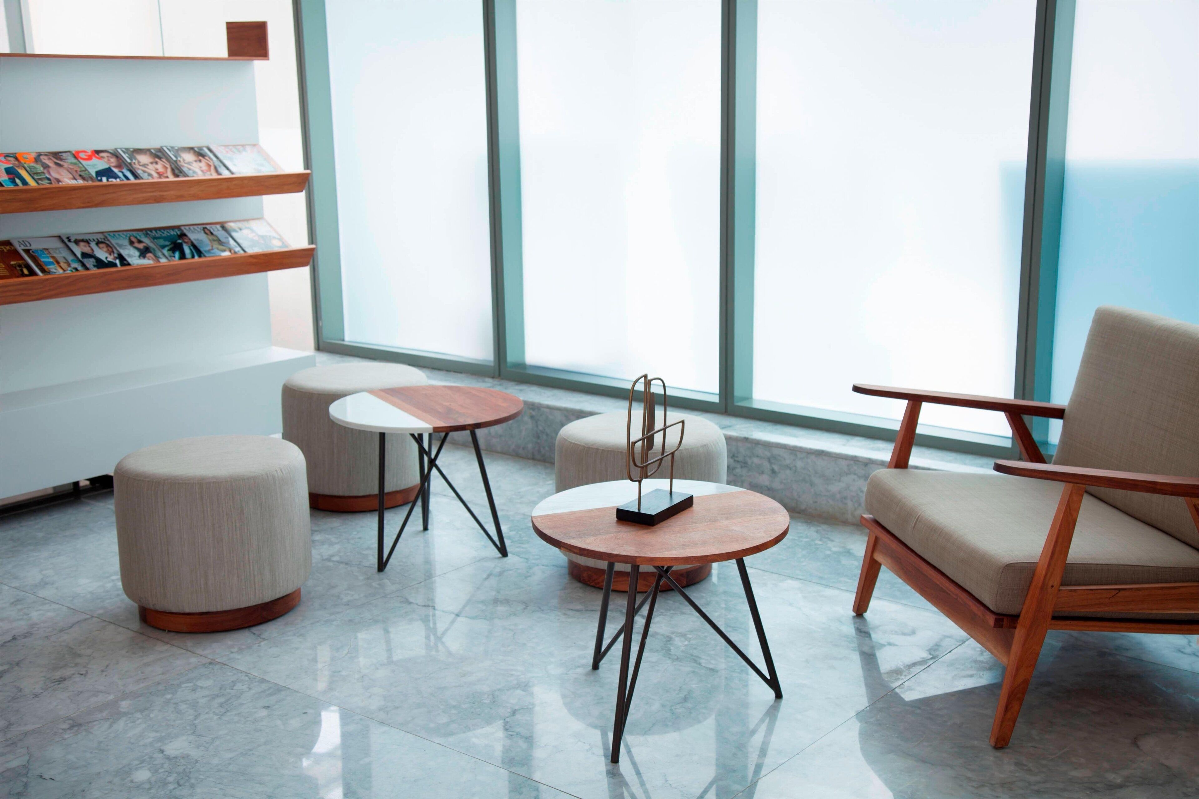 A modern lounge area with a wooden chair, ottoman, and round tables.