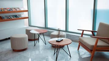A modern lounge area with a wooden chair, ottoman, and round tables.