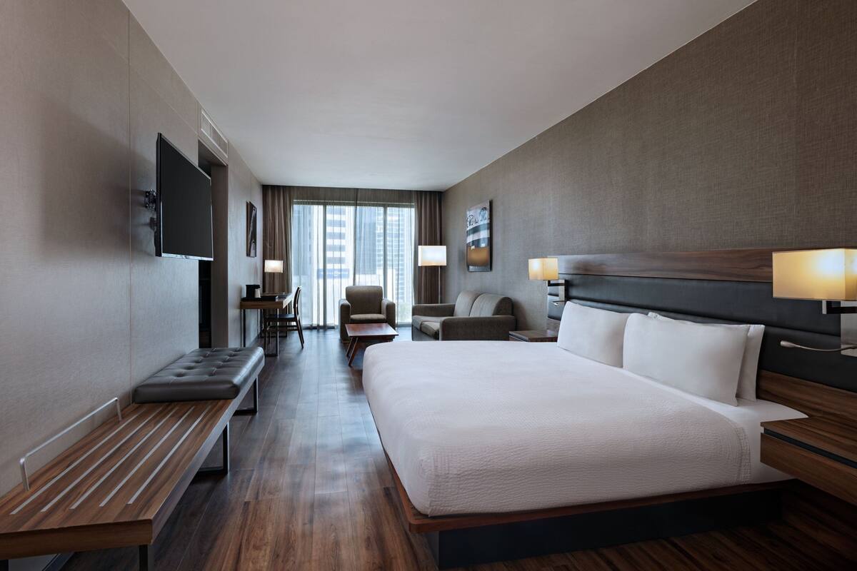 A modern hotel room with a large bed, a desk, a chair, and a TV mounted on the wall.