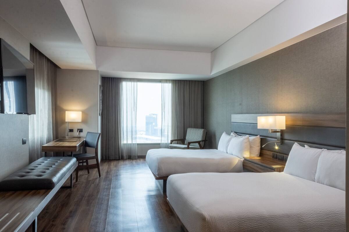 Une chambre d’hôtel avec deux lits, un bureau, une chaise, une télévision et une fenêtre avec des rideaux.