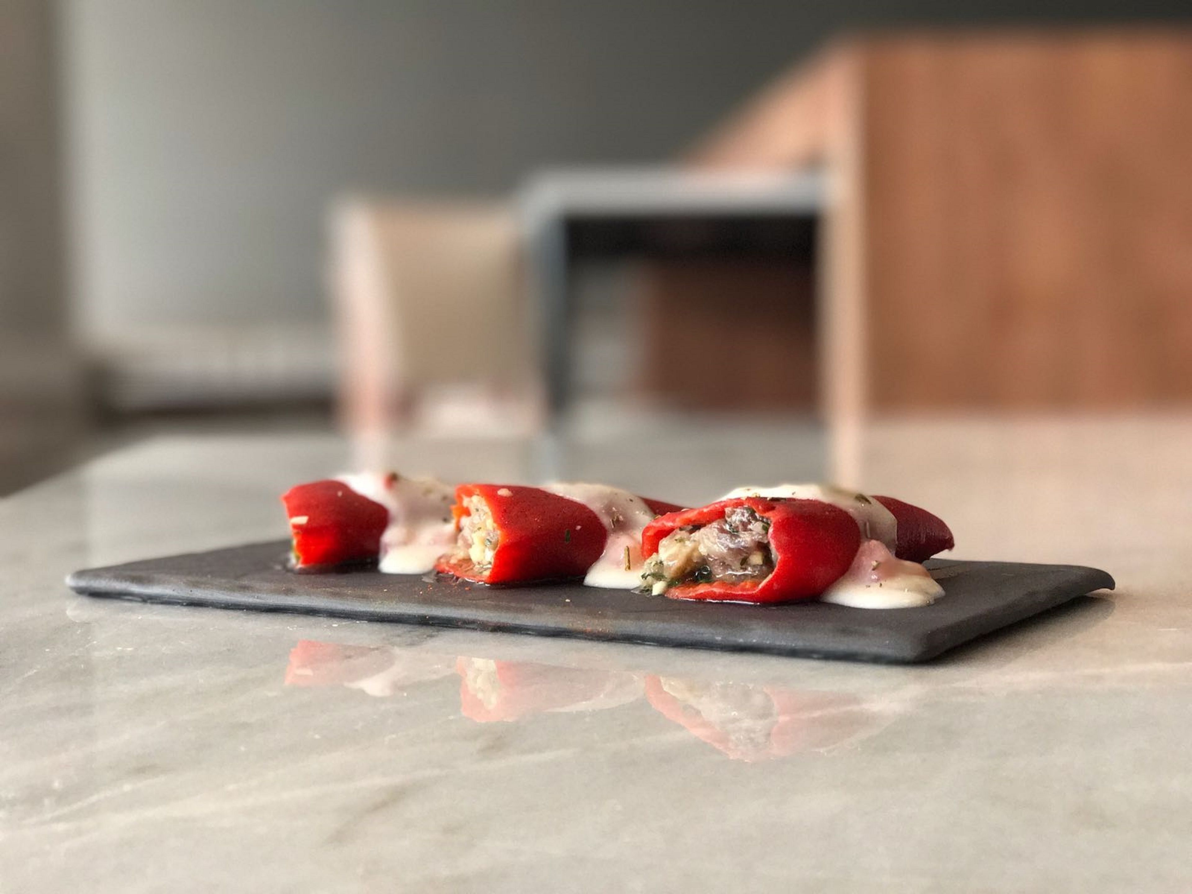 A black slate serving tray with a red stuffed pepper appetizer and a white sauce on a marble countertop.