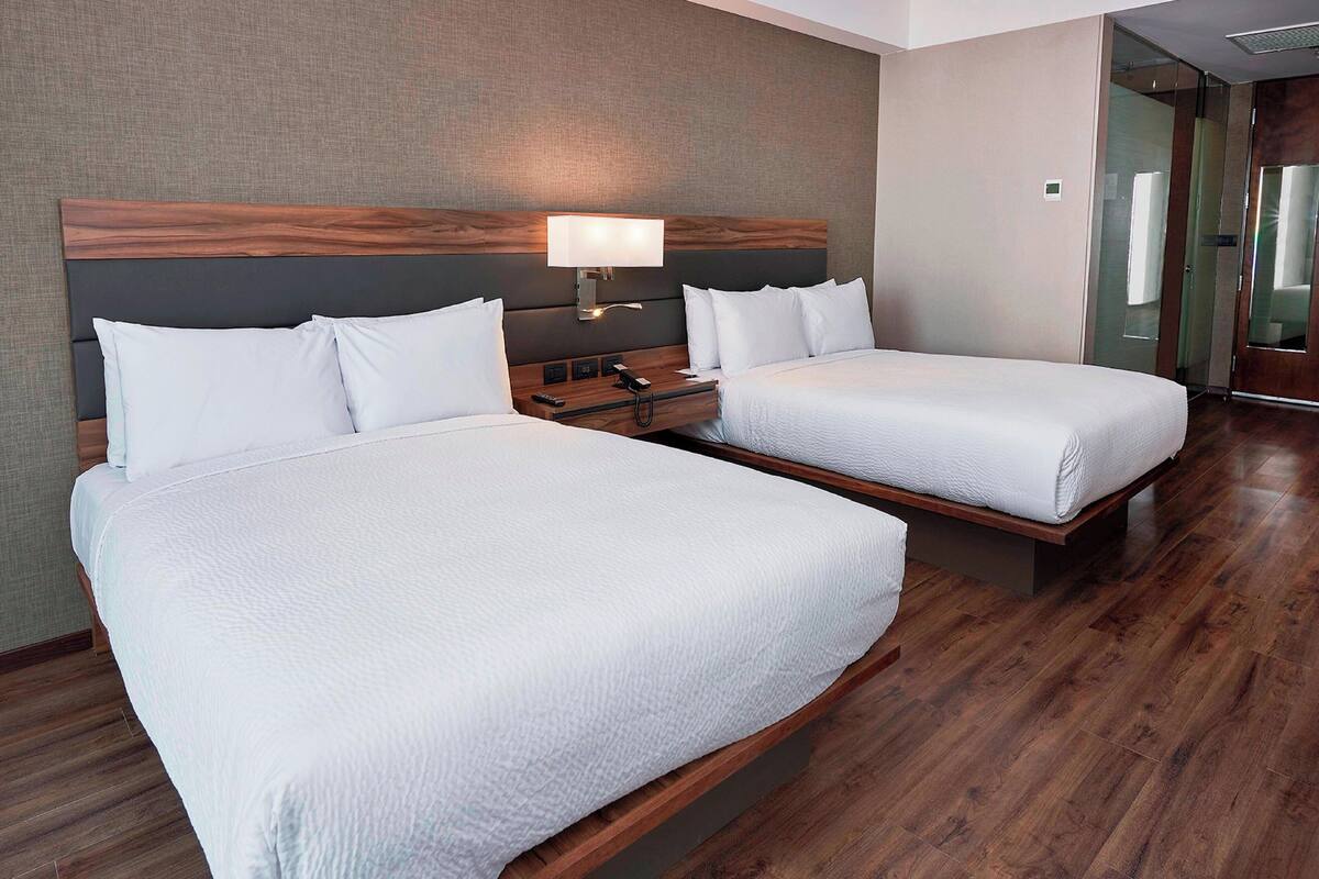 Une chambre d’hôtel avec deux lits, une table de chevet, une lampe et une tête de lit en bois.