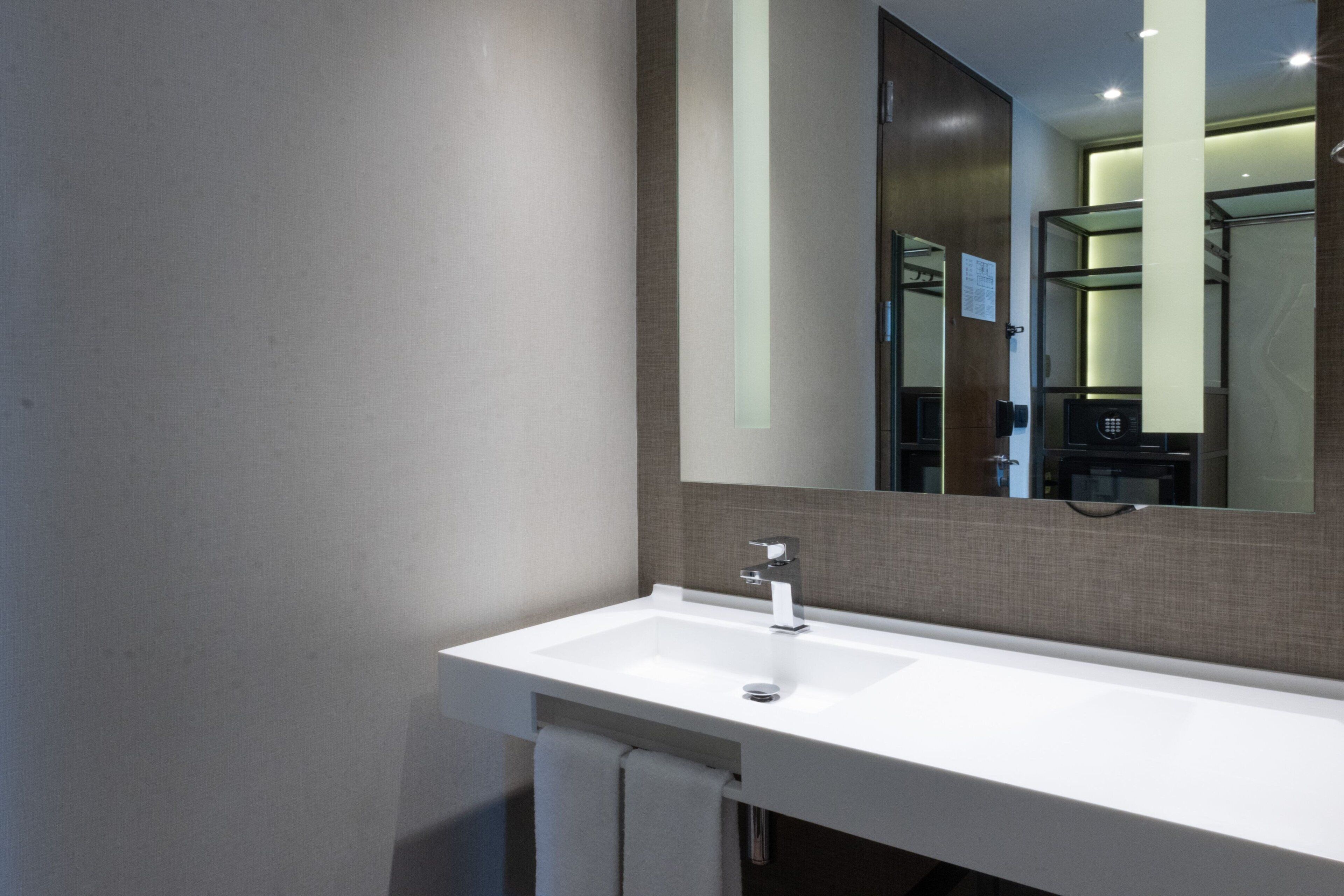A modern bathroom with a white sink, a large mirror, and a towel hanging on the wall.
