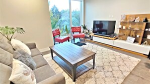 A modern living room with a sofa, coffee table, and red chairs. A TV is mounted on the wall, and there's a bookshelf with decorative items. - Monki Di Executive Suites - GLAS - Luxury Inner City Home 3 min to Downtown w Private Rooftop Patio Fireplace (Calgary)