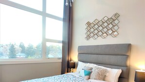 A modern bedroom with a large bed, a geometric-patterned bedspread, a decorative wall piece, and a ceiling light fixture. - Monki Di Executive Suites - GLAS - Luxury Inner City Home 3 min to Downtown w Private Rooftop Patio Fireplace (Calgary)
